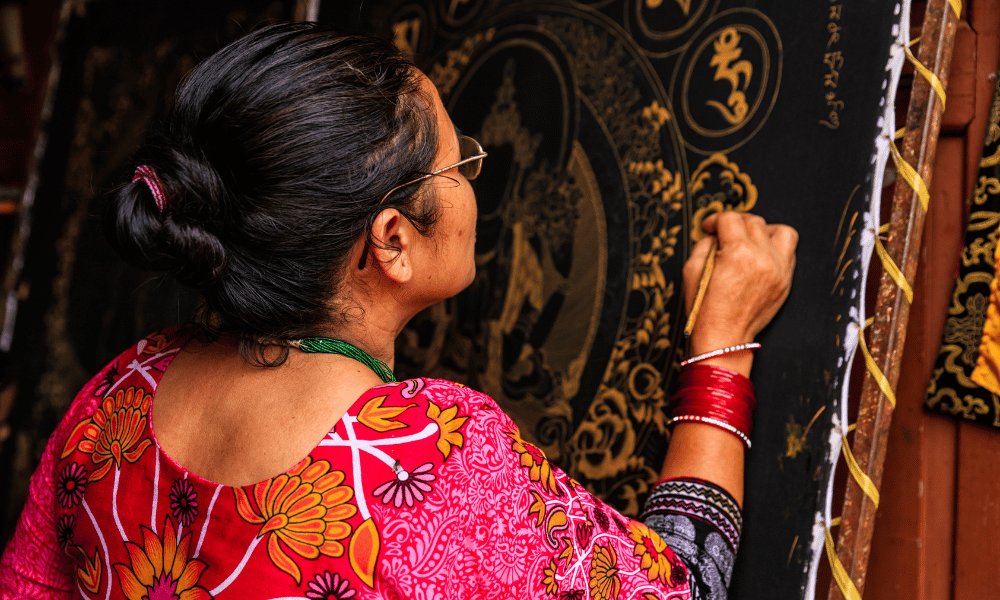 an artisian finishing off a thangka painting with gold outlines