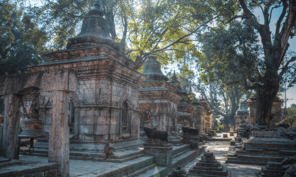 Shivalaya surrounded by trees and a bell infront of it